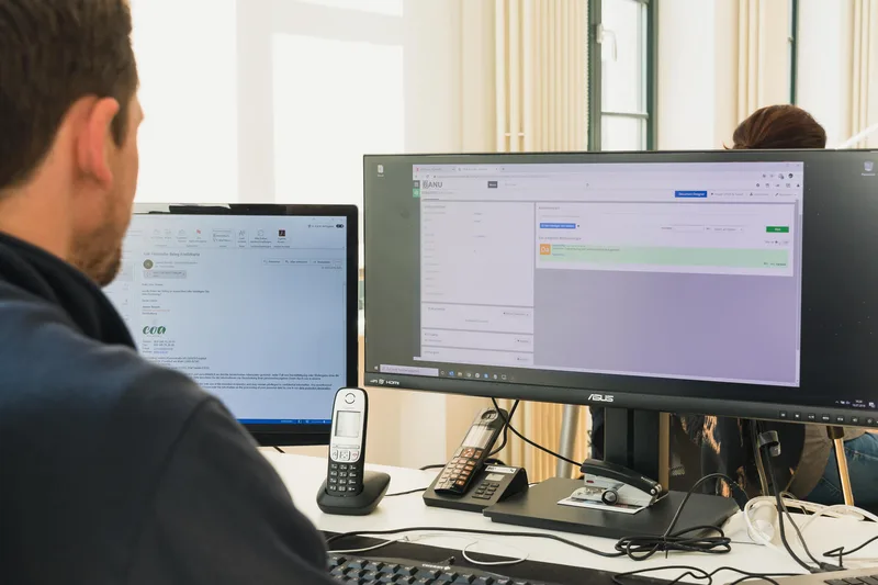 Person an einem Bildschirmarbeitsplatz, auf dem Monitor eine Systemoberfläche.
